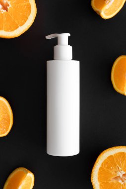 Siyah arka planda portakallarla çevrili beyaz bir kozmetik şampuan şişesinin üst görüntüsü..