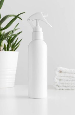Beyaz kozmetik tetik sprey şişesi, beyaz bir masa üzerinde aloe vera ve havlular..