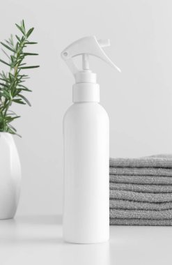 Beyaz kozmetik tetik sprey şişesi havluyla ve beyaz bir masada biberiye..