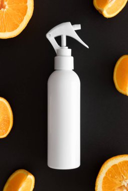 Siyah zemin üzerinde portakallarla çevrili beyaz bir kozmetik püskürtücü şişesinin üst görüntüsü.