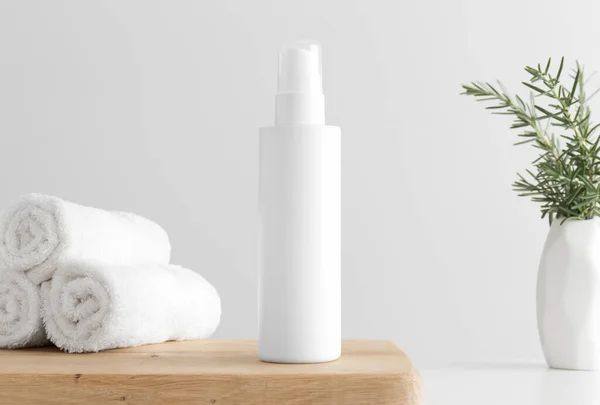 White cosmetics lotion bottle mockup with towels and a rosemary on a wooden table.