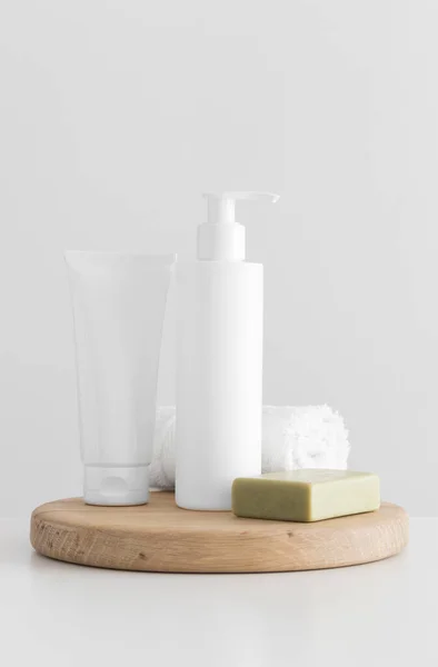 White cosmetic bottle and a tube of cream mockup with a natural soap and a towel on a white table.