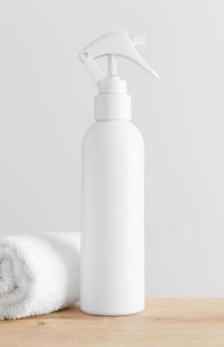 Beyaz kozmetik tetik sprey şişesi ahşap bir masada havluyla hazırlanıyor..