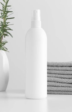 Beyaz kozmetik sprey şişesi, beyaz bir masa üzerinde havlu ve biberiye..