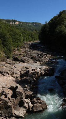 Net, engebeli bir dağ nehri, büyük kaba kayaların arasında, güzel bir plato manzarasının ve parlak mavi bir gökyüzünün zeminine karşı kaynıyor.