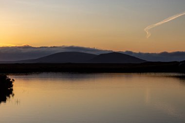 Kuzey Uist Hebridean adasında gün batımında sakin bir göl manzarası.