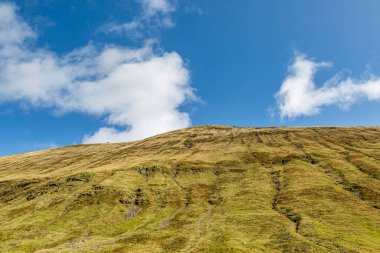 İskoçya 'nın dağlarındaki engebeli bir dağa bakıyorum, tepede mavi bir gökyüzü var.