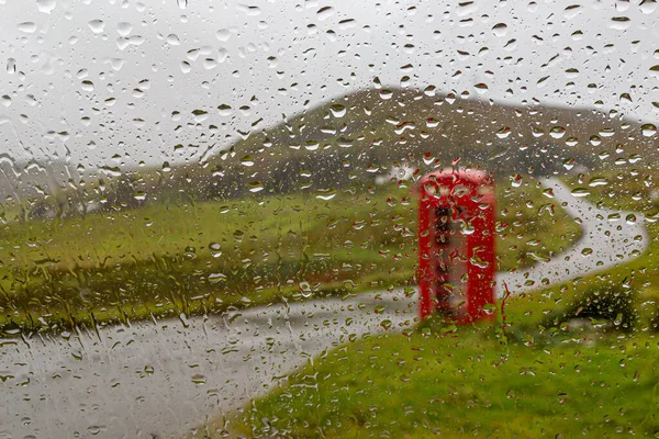 Looking through a window covered in raindrops at a telephone box in the Isle of Skye countryside