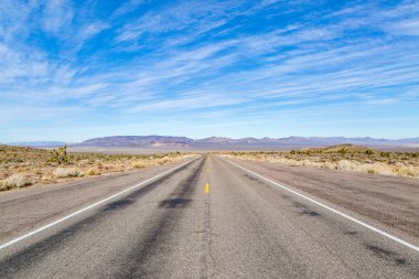 Nevada 'nın ücra bir köşesinde, üzerinde mavi bir gökyüzü olan uzun bir yol.