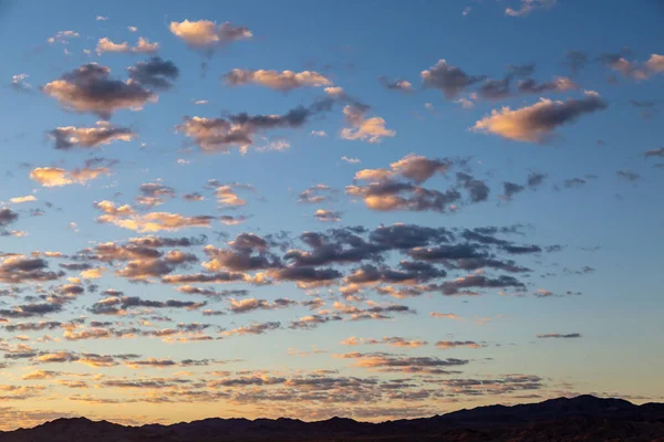 Silhouetted hills at sunrise, with light reflecting off fluffy clouds