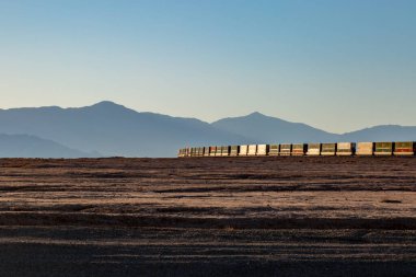 Uzaklarda siluetli tepeleri olan uzak bir Kaliforniya manzarasında seyahat eden bir tren.