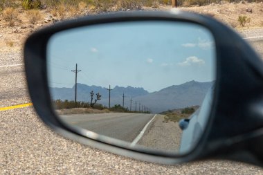 Bir arabanın dikiz aynasına bakıyorum, yol boyunca telgraf direkleriyle ve manzaralı bir çöl manzarasıyla.