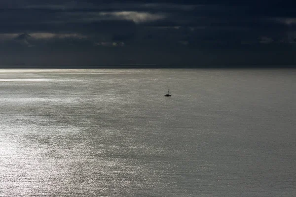 穏やかな海に浮かぶ帆船で 水面には太陽の光が差し込みますが 頭上には暗い雲が広がっています — ストック写真