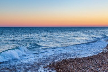 Brighton 'daki çakıl taşı plajı. Tepesinde günbatımı gökyüzü var.