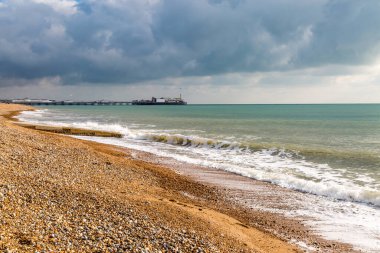 Brighton sahilinin üzerinde bulutlu bir gökyüzü, uzaktaki rıhtımla