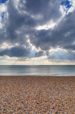 Brighton 'daki çakıl taşı plajı. Bulutlarda güneş ışınları parlıyor.