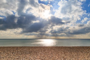 Brighton 'daki çakıl taşı plajı. Bulutların arasında güneş parlıyor.