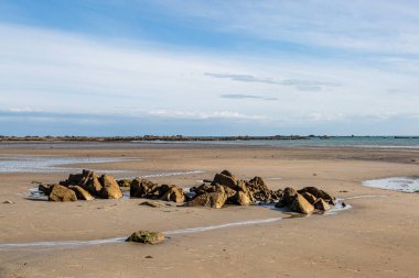 Güneşli bir yaz gününde Jersey adasında kumlu bir sahilde kayalar.