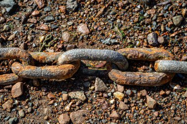 Çakıl taşına dayanan paslı metal bir zincir.