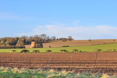 Güneşli bir kış gününde sürülen tarlalarda bir saman yığını.