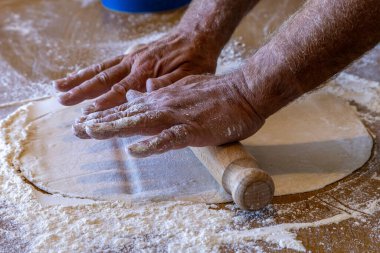 A pizza base being rolled out  with a rolling pin, with selective focus