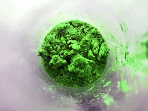 Green powder in glass cup, bowl with ingredient close up. colored granules in transparent container. Magic fantasy powder. Alchemy and elements. top view