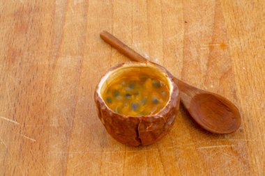 Maracuja, tahta kaşık ve ahşap arka planda yaprak ile küçük cam kabuk içinde ikiye bölünmüş. Meyve suyu ve çekirdekli tutku meyvesi.