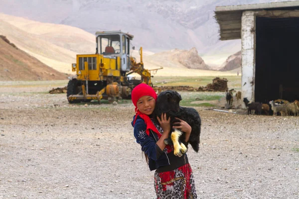 TAJIKISTAN, 23 Temmuz 2018: Pamir Otoyolu 'ndaki uzak dağ yerleşimlerinde yaşayan, Kırgız etnik kökenli keçi çocukla oynayan kız