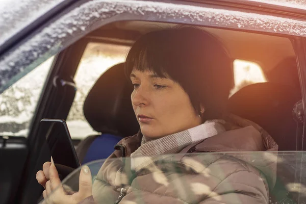 A woman sitting in the driver's seat and looking at the phone, close-up