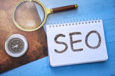 Harita ve büyüteç yanındaki mavi ahşap bir masa üzerinde bir not defteri ile Seo metin yatıyor