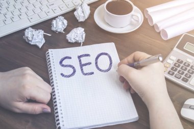 Bir kadın bir fincan kahve yanında ahşap bir masa üzerinde yatıyor bir defter bir Seo kaydı yapar.