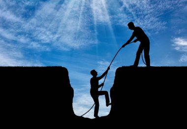 Bir siluet bir adamın başka bir çukurun dışına alınmasına yardımcı olur. Takım çalışması ve karşılıklı yardımlaşma kavramı