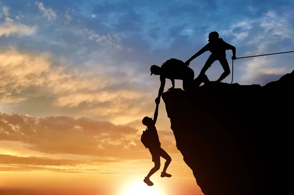 Başka bir erkek dağcı kolunu çekerek tahlisiye iki erkek dağcılar silüeti. Kavramsal sahne dağcılar yardım