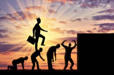 A selfish man with a crown on his head, walking on the heads of people as on the steps to the top. Conceptual scene of a narcissistic and selfish businessman clipart