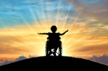 Günbatımında bir tepenin üstüne tekerlekli sandalyede oturan kız mutlu Engelli Çocuk silüeti. Engelli mutlu çocuk kavramı
