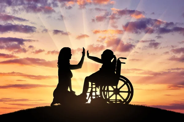 Silhouette of a happy disabled child girl sitting in a wheelchair and her mom beside. Concept of a happy family with a disabled child