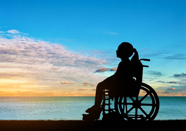 Silhouette of a disabled child girl sitting in a wheelchair looking at a sea sunset. Conceptual image of a girl with a disability