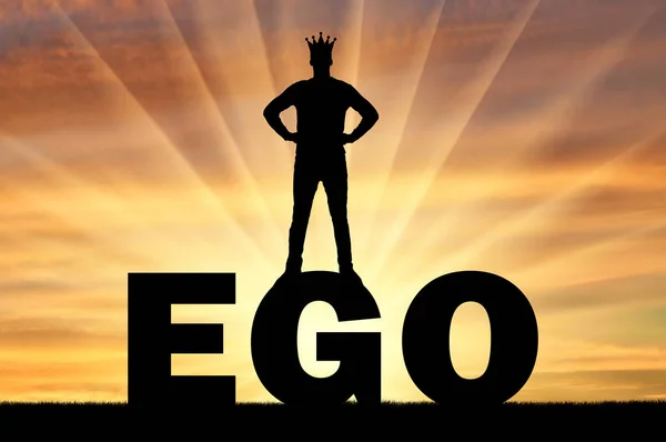 Silhouette eines Mannes mit Krone auf dem Kopf, der auf dem Wort Ego vor dem Hintergrund eines Sonnenuntergangs steht — Stockfoto