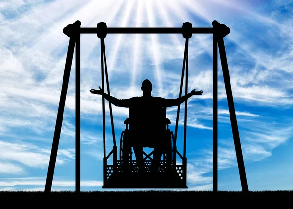 Silueta de un hombre feliz es una persona con discapacidad en una silla de ruedas en un columpio adaptativo para personas con discapacidad . — Foto de Stock