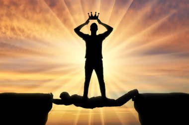 Selfish man puts a crown on his head, he stands on a man in the form of a bridge over a precipice clipart