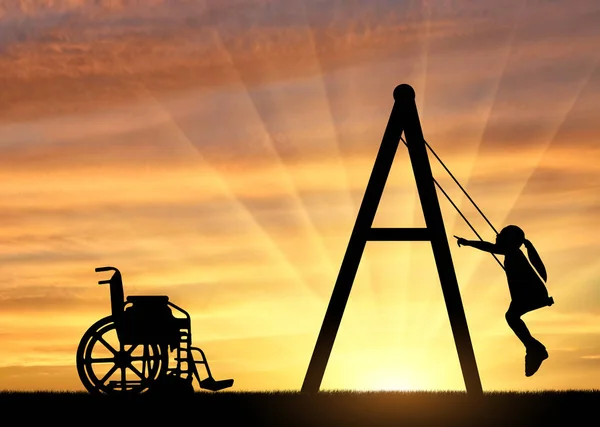 Silueta de una niña discapacitada en un columpio junto a una silla de ruedas sobre un fondo al atardecer — Foto de Stock