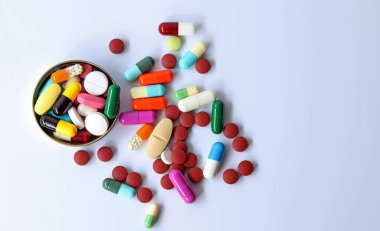 Şişenin kapağındaki ilaçların üst görüntüsü, renkli haplar, tabletler ve kapsüller beyaz arka planda izole edilmiş. Tıbbi klinikte, eczacılık hizmetlerinde ilaç reçeteli kullanımı.