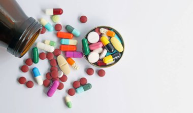 Şişenin kapağındaki ilaçların üst görüntüsü, renkli haplar, tabletler ve kapsüller beyaz arka planda izole edilmiş. Tıbbi klinikte, eczacılık hizmetlerinde ilaç reçeteli kullanımı.