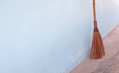 Kirli zemini temizlemek için kurutulmuş hindistan cevizi yapraklarından ve bambudan yapılmış süpürge sapı, dışarıyı paspaslamak için temizlikçi aracı, mavi duvar betonu, ev temizliği konsepti.