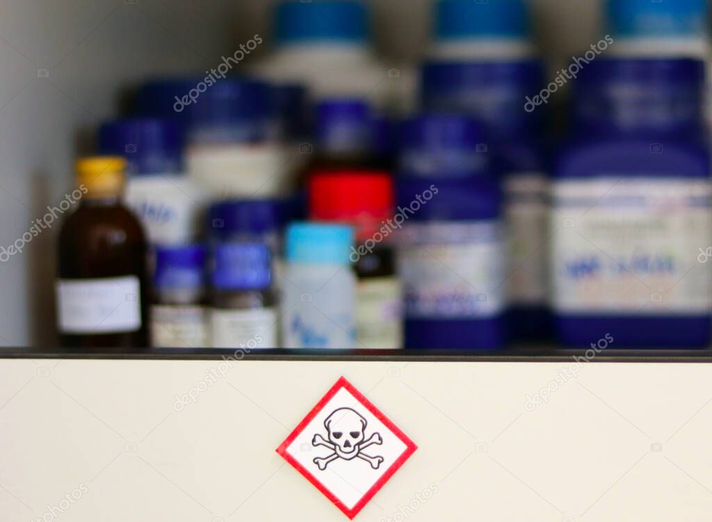 Chemical Hazard Sign pictogram, Globally Harmonized System of Classification and Labelling of Chemicals (GHS) Toxic category with container bottle on shelf cabinet, selective focus blurred background.