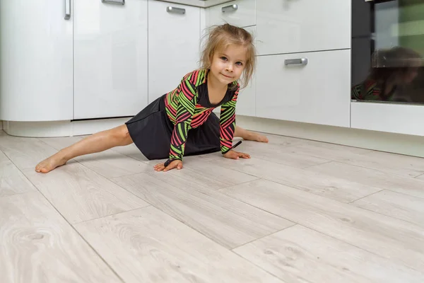 beautiful girl 4 years old in a gymnastic leotard is engaged in gymnastics at home in the kitchen.