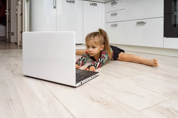 little girl doing gymnastics at home online. doing splits in front of laptop