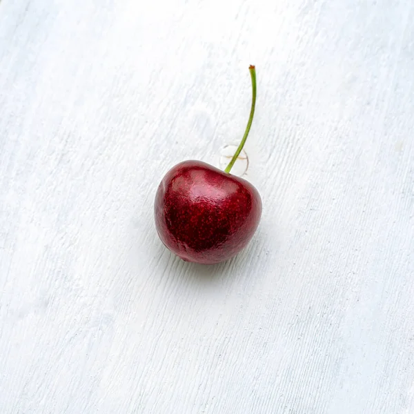 one ripe red cherries close-up on a white wooden textured background. copy space