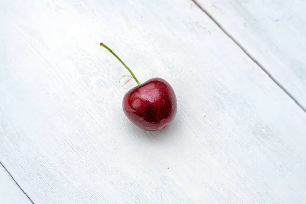 one ripe red cherries on a white wooden textured background. copy space