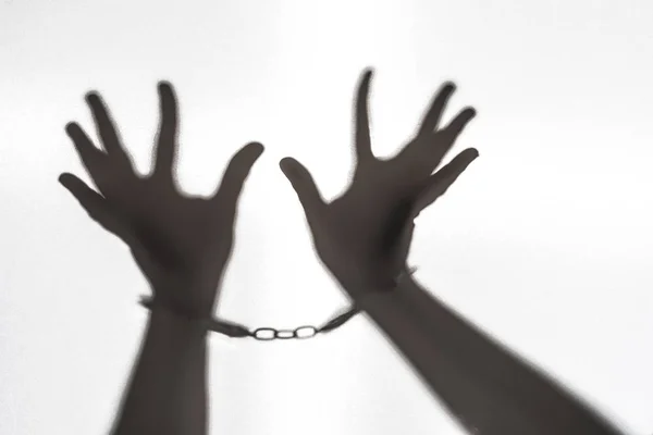 Hands of prisoner who calls for help. Silhouette of hand with handcuff on white background